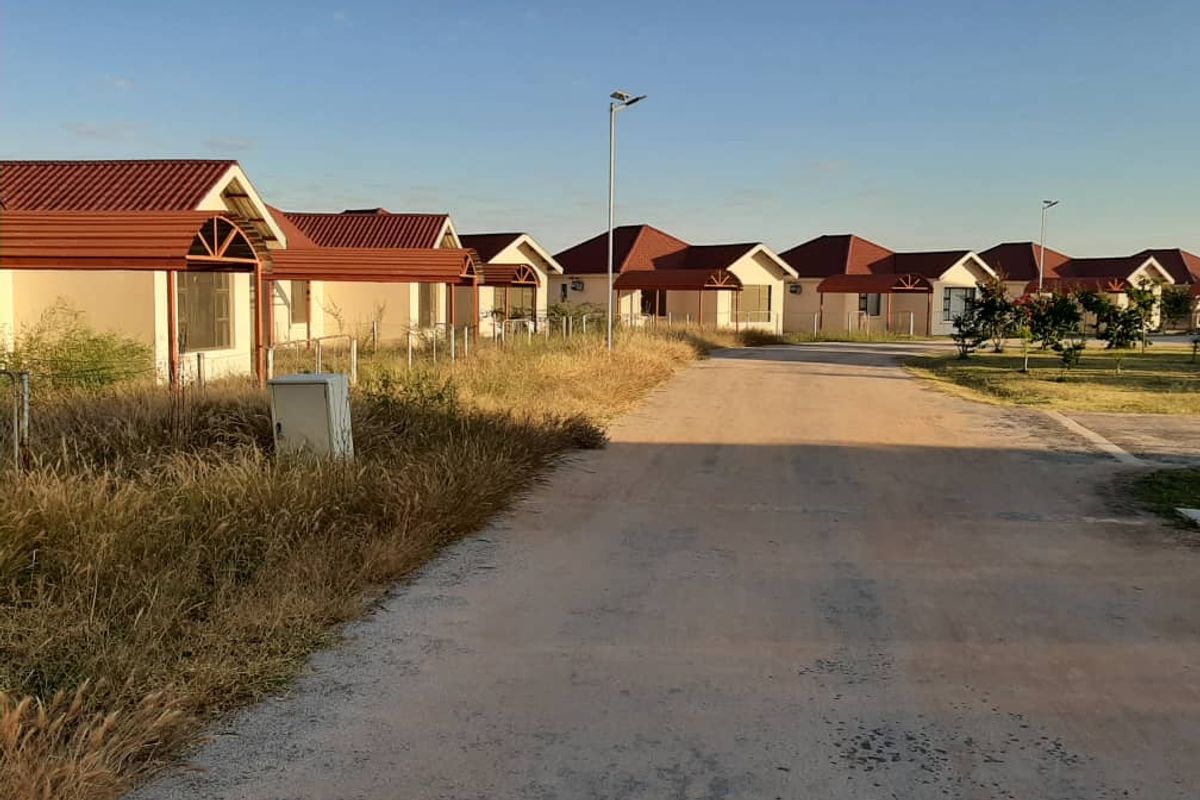 A street view of a residential development featuring multiple detached houses with tiled roofs and an unpaved access road.