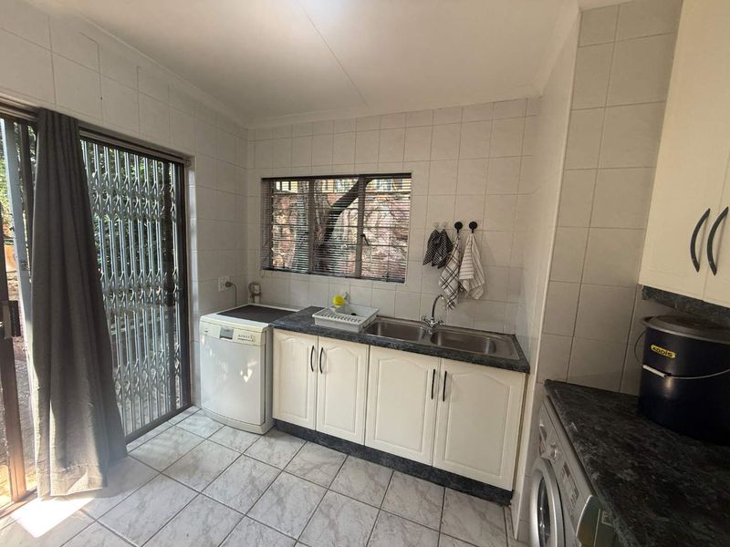 A functional laundry room featuring tiled walls and flooring, built-in cabinetry with a double basin sink, and direct access to the exterior via a sliding door.