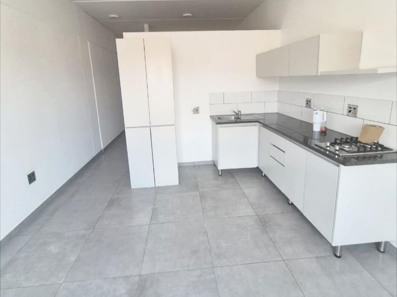 A modern, minimalist kitchen featuring white cabinetry, stone countertops, a gas hob, and neutral tiled flooring in an open-plan layout.