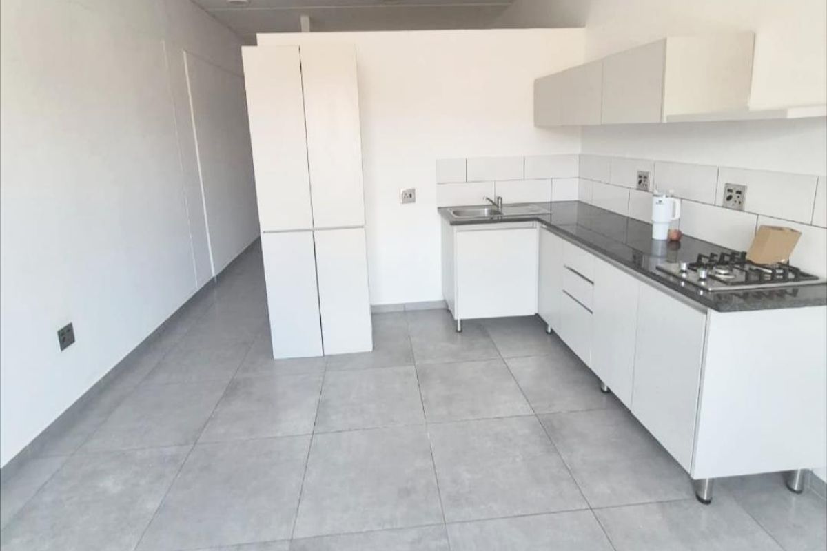 A modern, minimalist kitchen featuring white cabinetry, stone countertops, a gas hob, and neutral tiled flooring in an open-plan layout.
