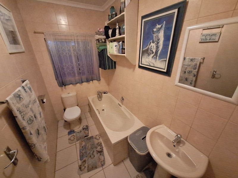 A functional bathroom featuring a built-in bathtub, pedestal basin, toilet, and full-height wall tiling.