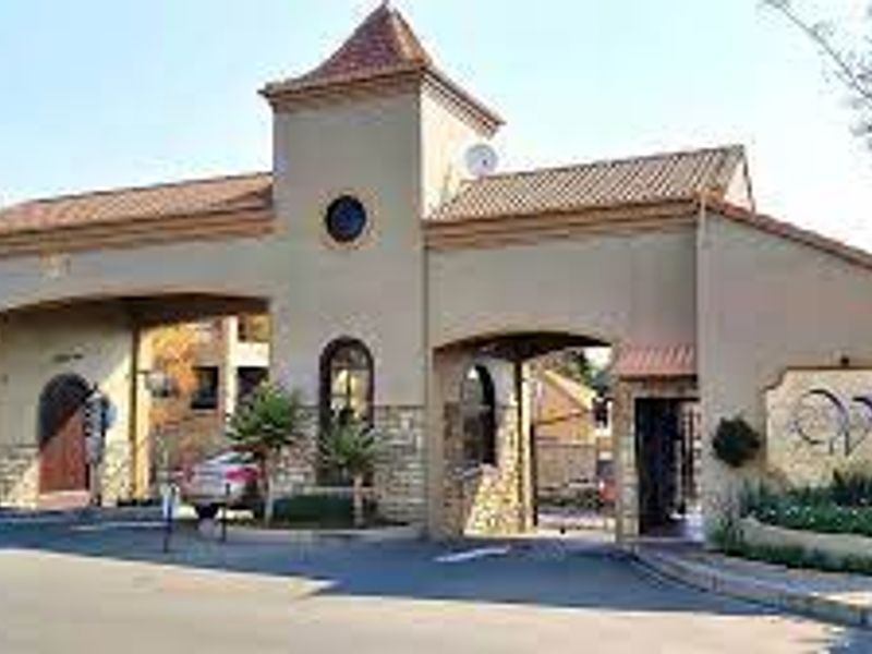 The main entrance gatehouse of the apartment complex featuring stone cladding, arched entryways, and a tiled roof structure.