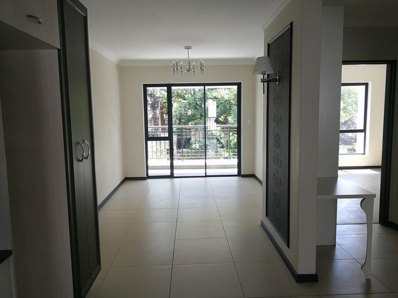 Spacious open-plan living area featuring neutral tiled flooring, modern lighting, and a sliding glass door leading to a balcony.