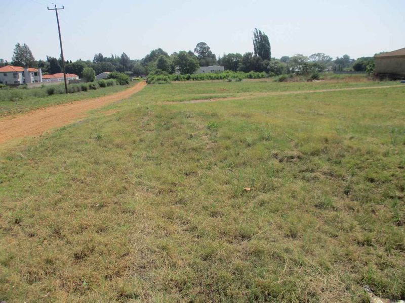 A vacant residential plot featuring natural grassland, dirt road access, and existing utility infrastructure nearby.