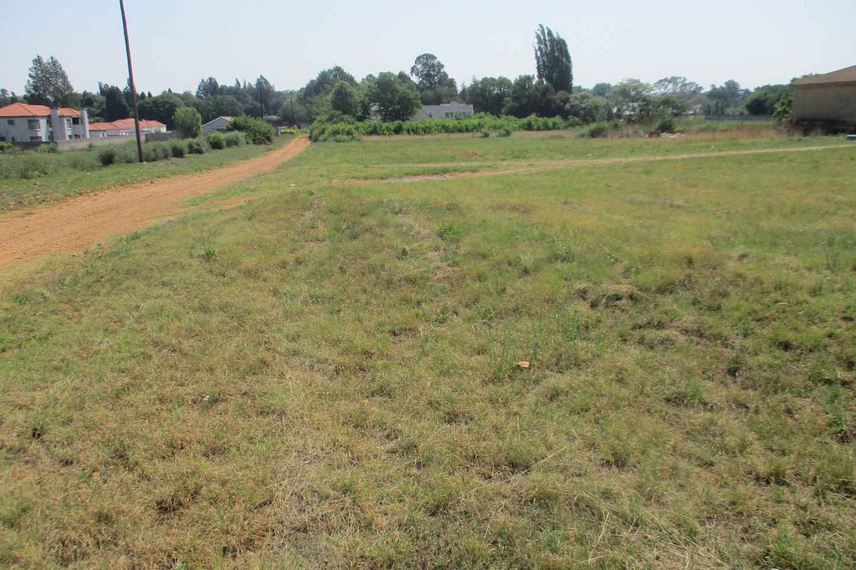 A vacant residential plot featuring natural grassland, dirt road access, and existing utility infrastructure nearby.