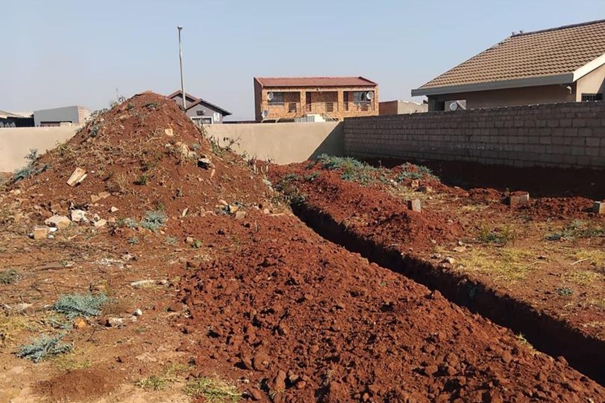 A vacant residential plot featuring an excavated foundation trench and perimeter boundary wall, showing active site preparation for construction.
