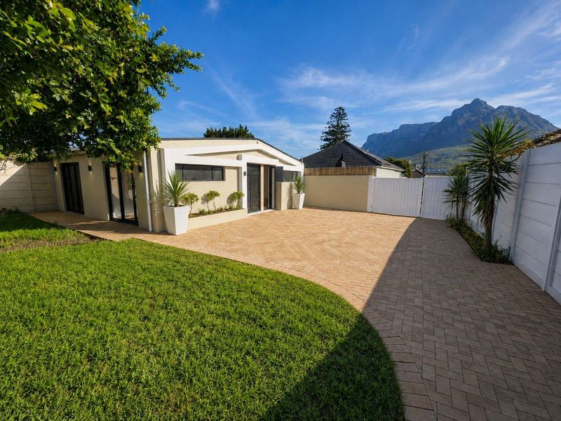 A well-maintained rear exterior featuring a paved courtyard, manicured lawn, and mountain views, providing a clean and inviting outdoor space.
