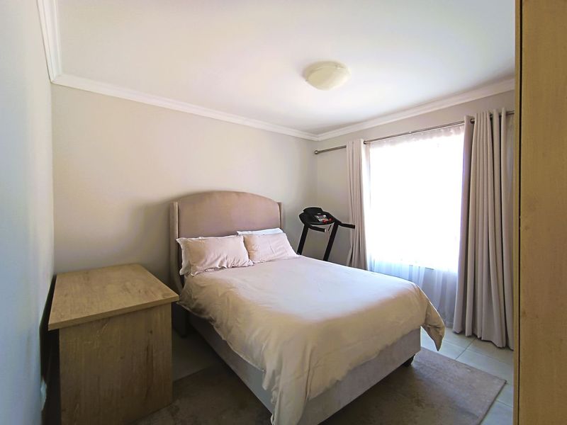 A functional bedroom featuring tiled flooring, neutral wall tones, and a window with fitted curtain rods, offering a clean and simple living space.