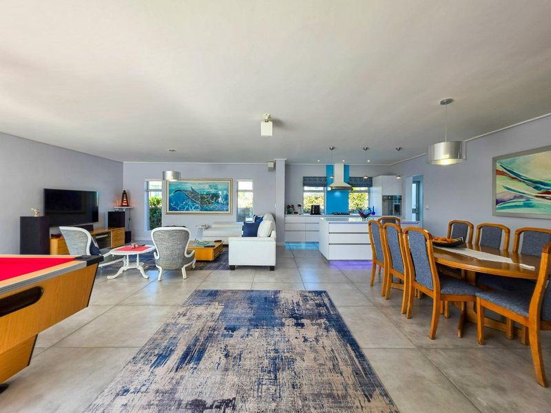 Spacious open-plan living area featuring a modern kitchen with a central island, dining space, and lounge, all finished with neutral floor tiles.
