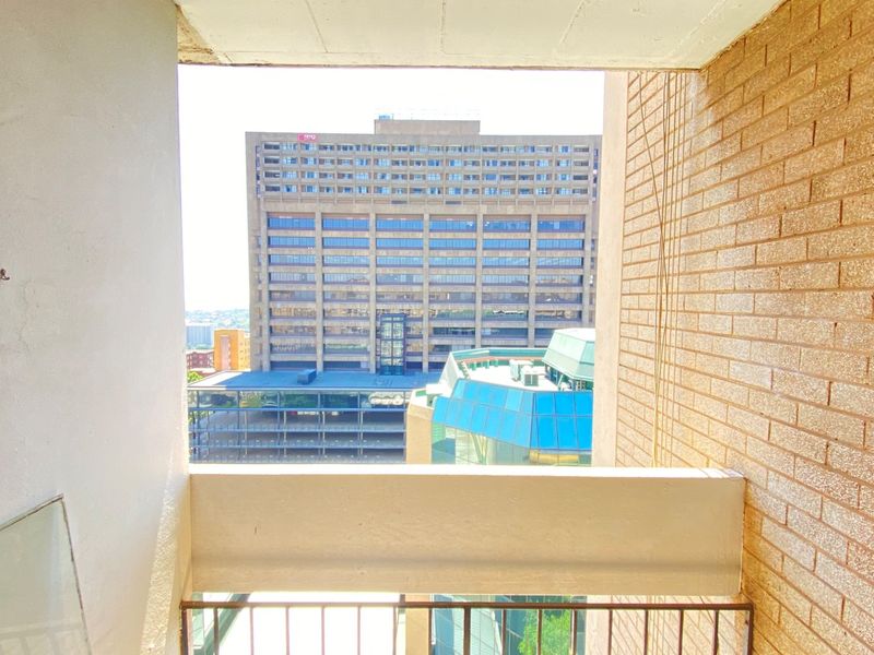 A compact balcony featuring a brick wall and metal railing, offering an urban view of the surrounding city buildings.