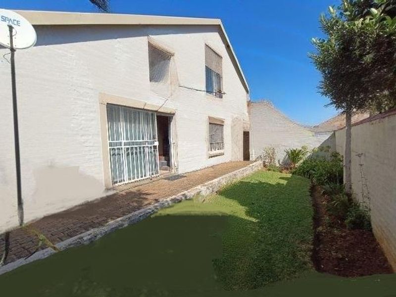 Rear view of the townhouse featuring a paved walkway, small lawn area, and secure access point with a security gate.