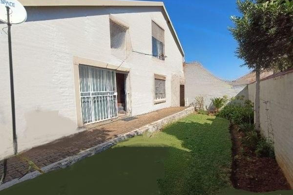 Rear view of the townhouse featuring a paved walkway, small lawn area, and secure access point with a security gate.