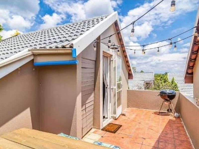 An open-air balcony featuring tiled flooring, a pitched roof structure, and overhead string lighting, providing a private outdoor space.