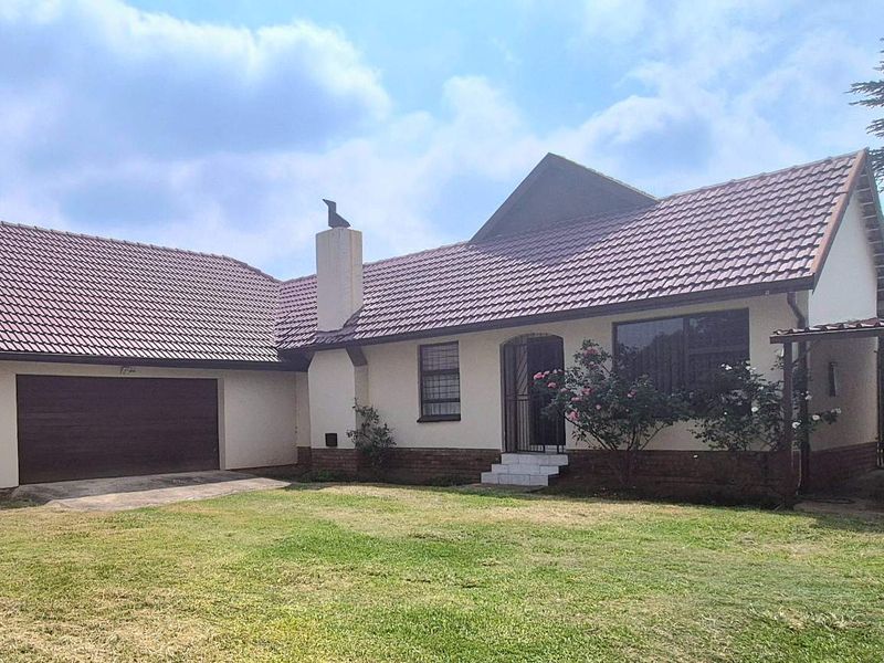 Front view of a well-maintained house featuring a tiled roof, attached double garage, paved driveway, and a covered carport area.