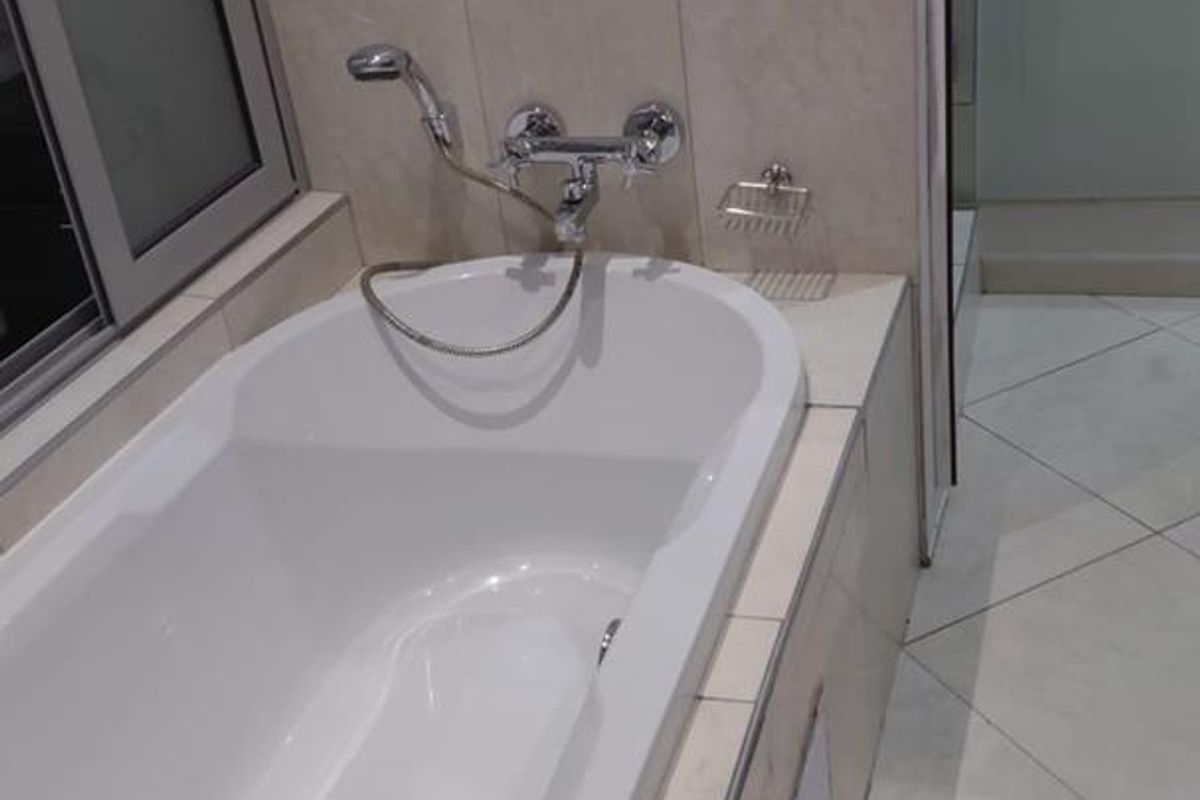 A clean bathroom featuring a built-in bathtub with chrome fixtures, tiled surround, and diagonal floor tiling.