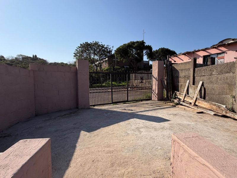 An exterior view of a townhouse driveway featuring a concrete boundary wall and a metal entrance gate.