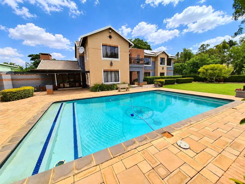 Spacious rear garden featuring a large swimming pool, paved patio area, and a covered outdoor entertainment space attached to the main residence.
