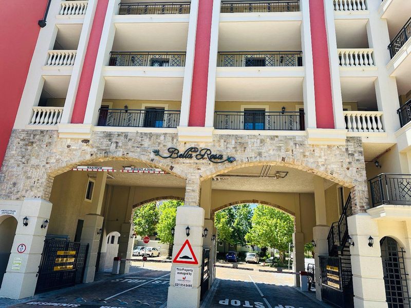 Front entrance facade of the Bella Rosa apartment complex featuring stone-clad arches, secure gated access, and multiple levels of balconies with wrought iron railings.
