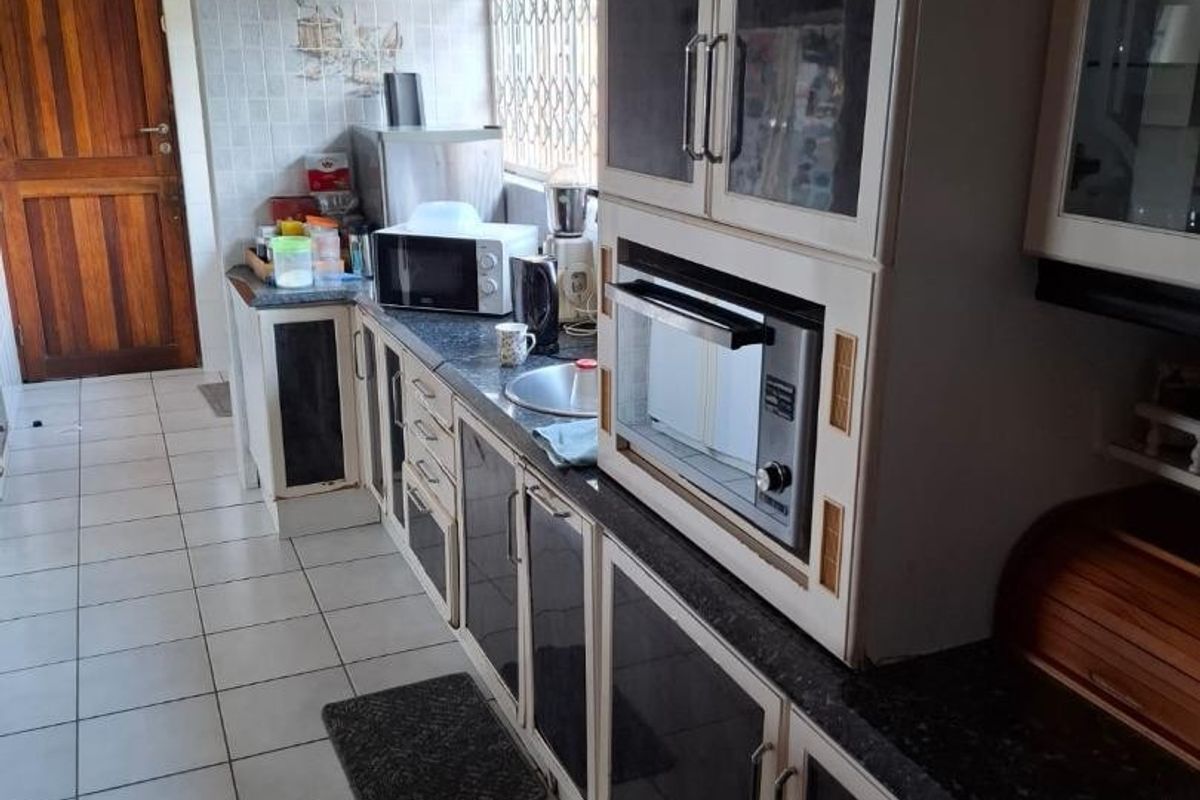 A functional kitchen featuring built-in cabinetry, a wall-mounted oven, tiled flooring, and a tiled splashback, offering a practical layout with potential for modern updates.