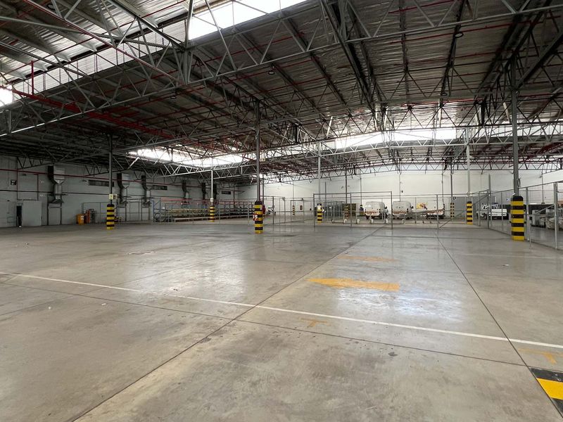Spacious industrial warehouse featuring high exposed steel truss ceilings, polished concrete flooring, integrated skylights, and secure partitioned storage areas with safety bollards.