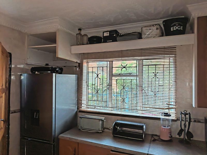 A kitchen area featuring tiled walls, laminate countertops, and window security bars, currently showing signs of wear and missing cabinetry components.