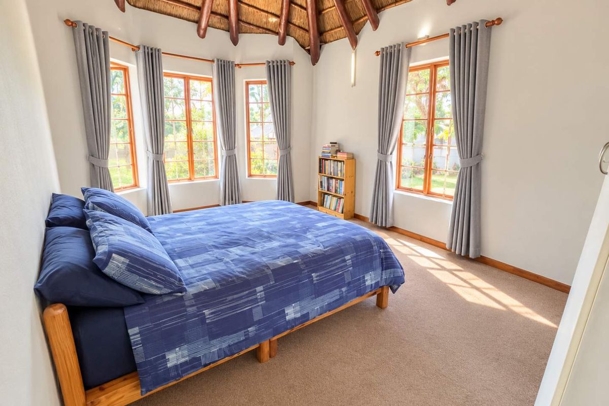 A bright bedroom featuring a unique vaulted thatched ceiling with exposed timber rafters, large wooden-framed windows, and neutral carpeting.