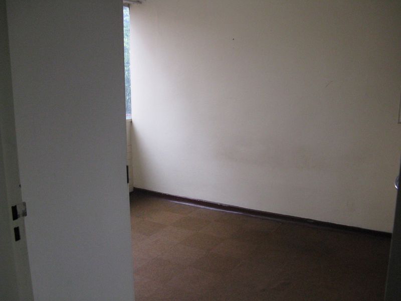 An empty bedroom featuring plain walls and dark flooring, offering a blank canvas for renovation or interior design updates.