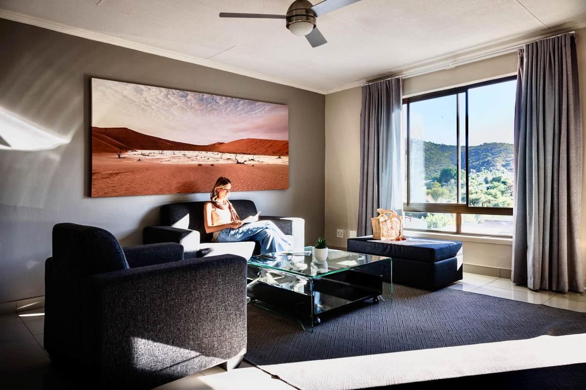 A comfortable living room featuring a ceiling fan, large window with natural light, and neutral wall tones, creating a bright and inviting space.