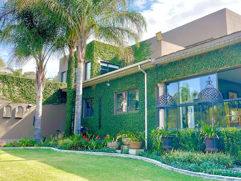 A well-maintained rear exterior view featuring a lush creeper-covered facade, large glass doors, and a manicured garden with mature palm trees.
