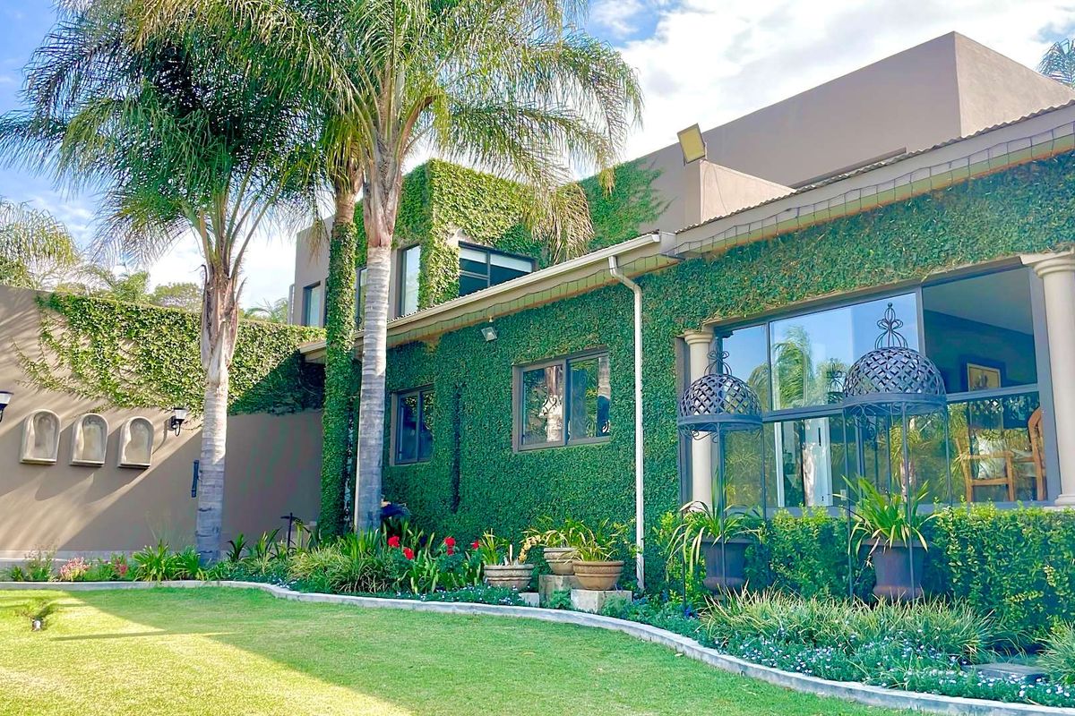 A well-maintained rear exterior view featuring a lush creeper-covered facade, large glass doors, and a manicured garden with mature palm trees.