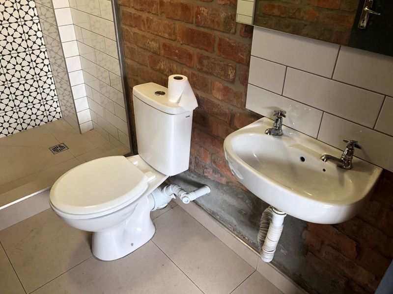 A bathroom featuring an exposed brick wall, a wall-mounted basin, and a tiled shower enclosure with visible plumbing fixtures.
