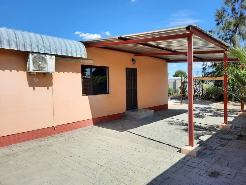A paved outdoor patio area featuring a covered roof structure, exterior wall-mounted air conditioning unit, and direct access to the home.