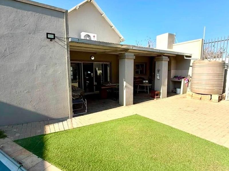 Rear exterior view featuring a covered patio, swimming pool, paved courtyard area, artificial lawn, and a water storage tank.