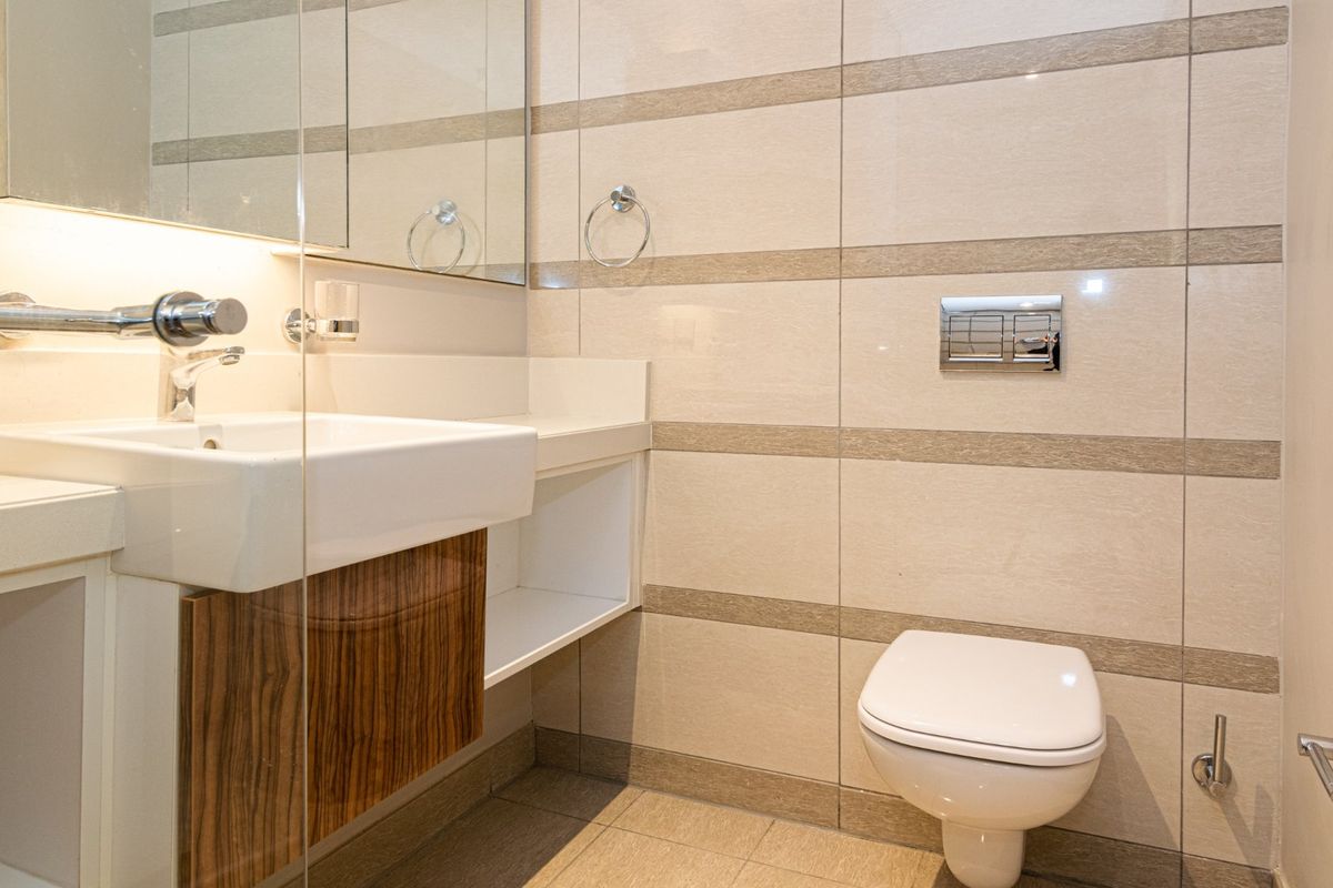 Modern bathroom featuring a wall-mounted toilet, floating vanity with integrated sink, glass shower partition, and neutral tiled walls.