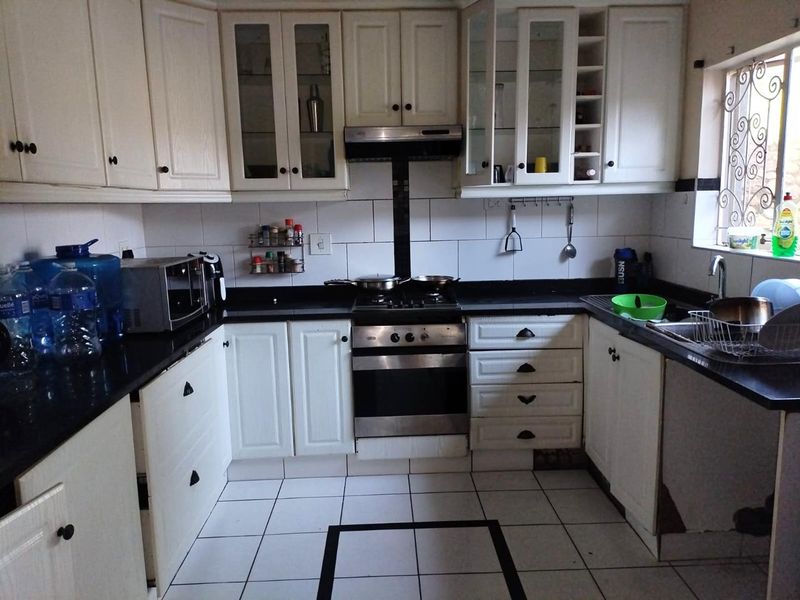 A functional kitchen featuring white cabinetry, black granite countertops, a gas stove with extractor fan, and tiled flooring with a decorative border.