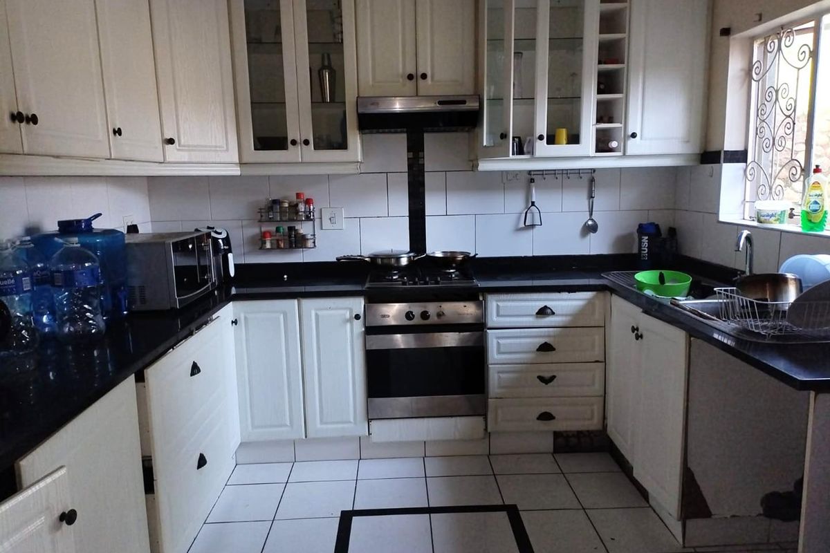 A functional kitchen featuring white cabinetry, black granite countertops, a gas stove with extractor fan, and tiled flooring with a decorative border.