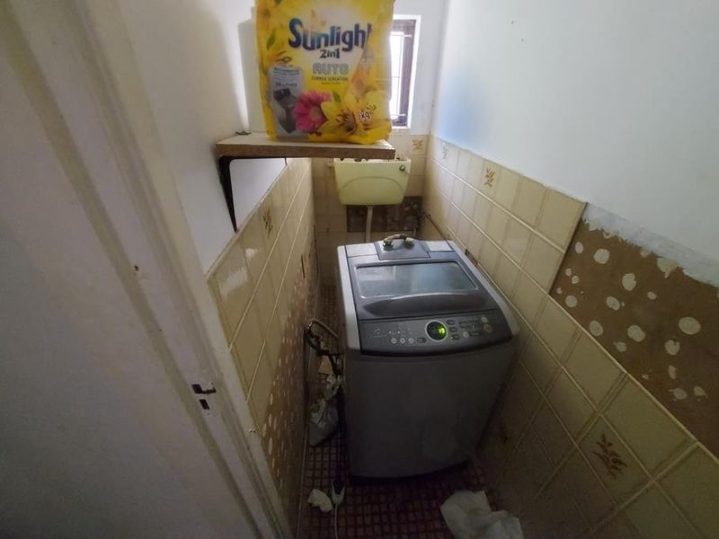 A small laundry area featuring wall tiling and plumbing connections, currently requiring maintenance and cosmetic repairs to the wall finishes.