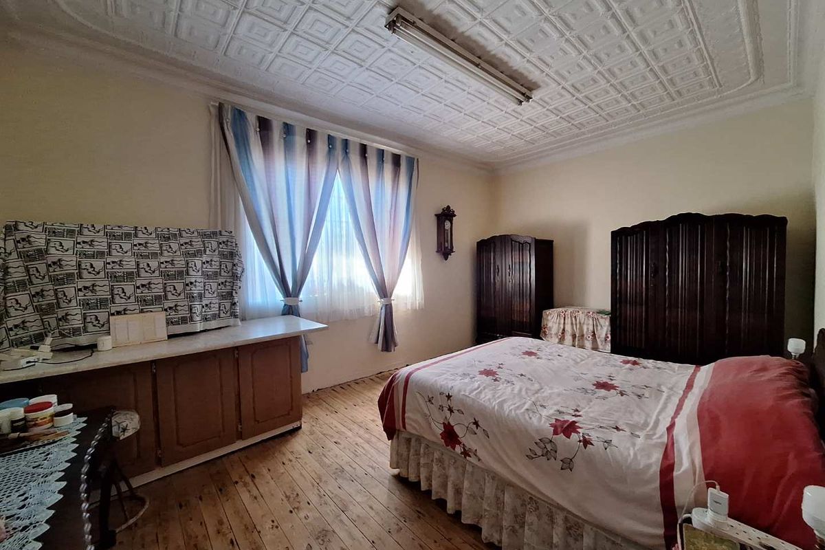 A bedroom featuring original timber flooring, a decorative pressed-tin style ceiling, and built-in cabinetry.