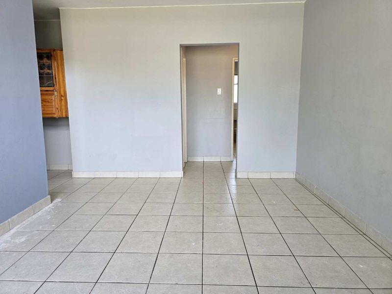 An empty living area featuring neutral grey walls and light-colored ceramic floor tiles, providing a blank canvas for interior design.