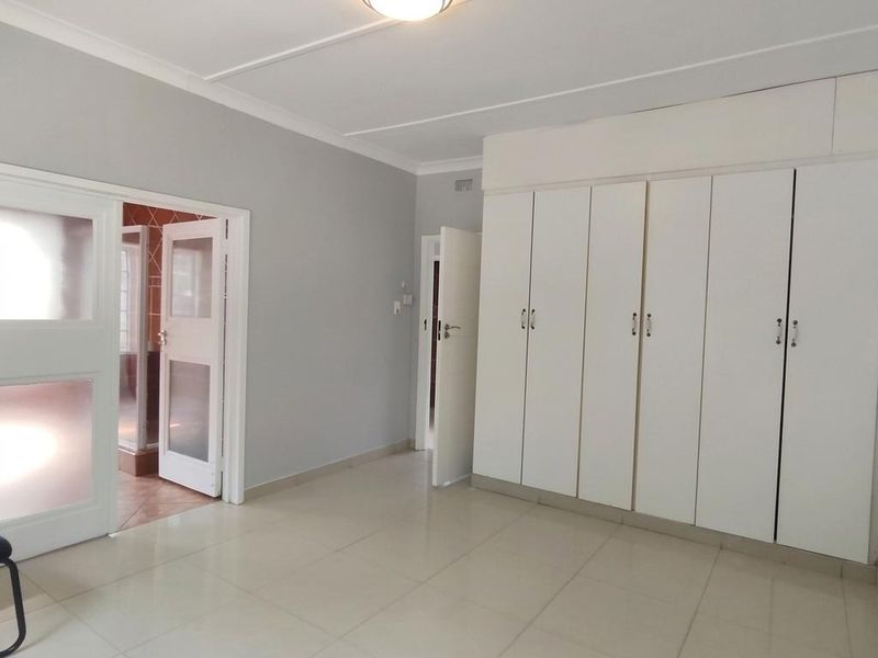 A spacious, empty bedroom featuring neutral tiled flooring, built-in cupboards, and direct access to an adjacent room.