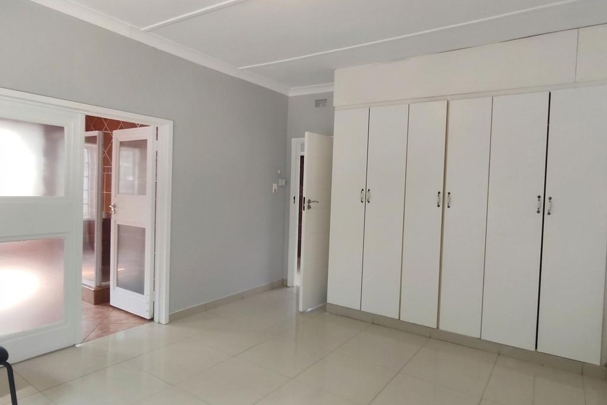 A spacious, empty bedroom featuring neutral tiled flooring, built-in cupboards, and direct access to an adjacent room.
