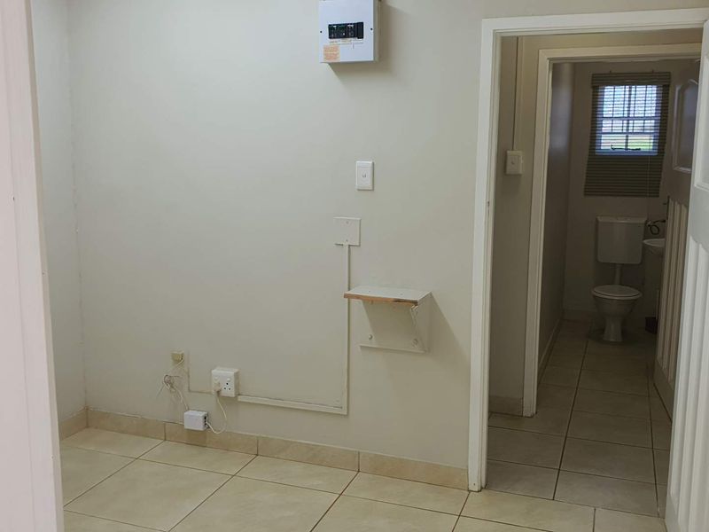 An empty office space featuring tiled flooring, an electrical distribution board, and direct access to an adjoining bathroom.