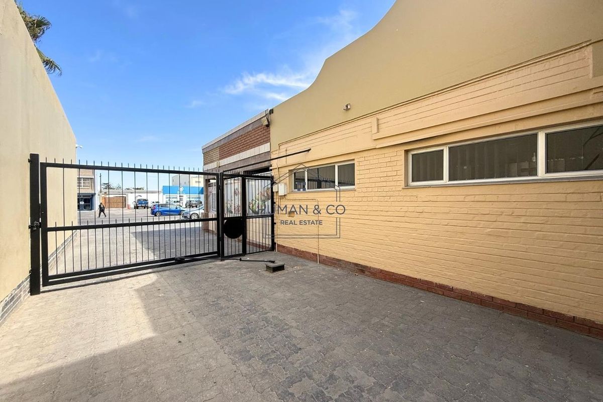 Exterior view of a commercial property featuring a paved courtyard, secure metal gate access, and painted brick facade with horizontal windows.