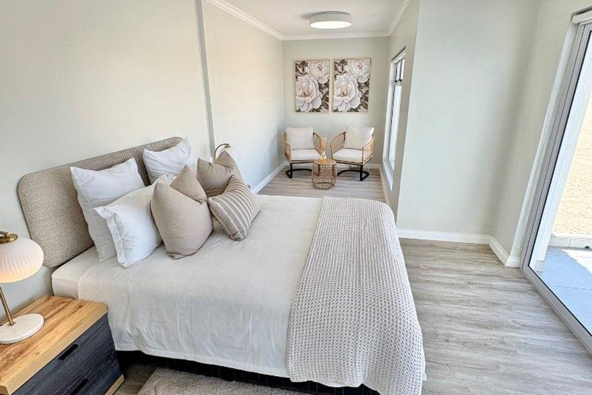 A bright and spacious bedroom featuring modern wood-look flooring, crown molding, flush-mount ceiling lighting, and large sliding glass doors leading to an outdoor area.