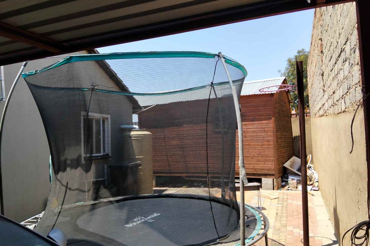 Rear outdoor area featuring a paved patio, a timber storage shed, a water tank, and a covered section, enclosed by a boundary wall.