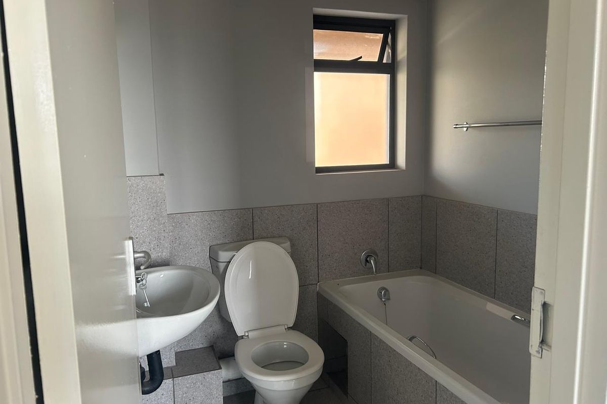 A functional bathroom featuring a bathtub, pedestal basin, and toilet with neutral wall tiling and a small window for natural light.