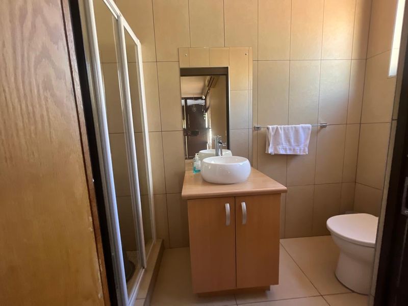 A functional bathroom featuring a vessel sink vanity, a glass-enclosed shower, and a toilet, finished with neutral wall and floor tiling.