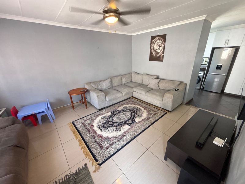 Open plan living area featuring tiled flooring and a ceiling fan, with an adjacent kitchen visible in the background.