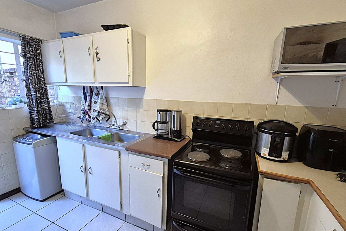 A functional kitchen featuring white cabinetry, a stainless steel double sink, a freestanding electric stove, and tiled flooring with a dedicated laundry appliance space.