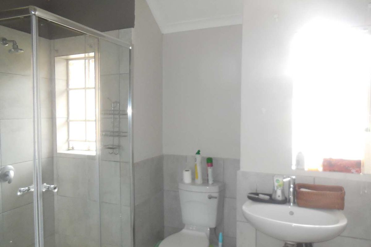 A functional bathroom featuring a glass-enclosed shower, a pedestal sink, and a standard toilet with neutral wall tiling.